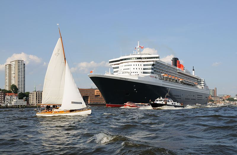 Fotos vom Kreuzfahrtschiff Queen Mary 2 QM2 auf der Elbe vor Hamburg Neumhlen.  011_60_4392 Viele Barkassen, Schiffe der Hafenrundfahrt und private Sportboote /  Motorboote begleiten den gewaltigen Luxusliner bei  seiner Fahrt auf der Elbe; ein Segelboot kreuzt vor dem Bug des Kreuzfahrtschiffs.Das britische Kreuzfahrtschiff  hat eine Lnge von 345 m und eine Breite von 45 m. Der Luxusliner bietet in 1310 Kabinen bis zu 2.620 Passagieren Platz und hat eine Besatzung von 1.253 Personen. Die Queen Mary 2 hat fnf Swimmingpools, einen Ballsaal, Golfanlage, Wintergarten, Sportzentrum, mit ber 8.000 Bchern die grte Bibliothek auf See, den grten ffentlichen Saal (Restaurant Britannia), der ber zwei Decks und die gesamte Schiffsbreite geht, acht weitere Restaurants, Fitness-Center, Planetarium, Kino, Theater.  www.hamburg-fotograf.com 