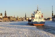 011_78_5837 Das 88 m lange und 12 m  breite Frachtschiff CAROLIN G. luft in den Hamburger Hafen ein. Die Elbe ist dicht mit Treibeis bedeckt. Die Abendsonnen scheint auf das Panorama mit den Trmen der Hansestadt Hamburg - ganz links der Kirchturm vom Hamburger Wahrzeichen die St. Michaeliskirche, auch Michel genannt; daneben die Spitze vom Rathausturm, die St. Petri-Kirche, die Jakobikirche, der Uhr- und Pegelturm der St. Pauli Landungsbrcken, die Gustav-Adolf-Kirche und im Bildzentrum der Turm der St. Nikolaikirche.