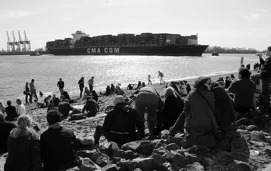 11_17450 Hamburger und Hamburgerinnen sitzen am Elbstrand bei der Strandperle und geniessen in der Abendsonne das faszinierende Schauspiel des Hamburger Hafens. Ein hoch beladenes Contaienrschiff wird auf der Elbe gewendet und mit Hilfe von Schleppern in den Waltershofer Hafen gebracht.   www.christoph-bellin.de