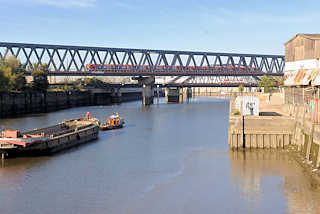 2660 S-Bahnzug in Fahrt auf der Eisenbahnbrcke ber den Oberhafenkanal / Billehafen in Hamburg Rothenbursort; eine Schute wird auf dem Kanal von einer Barkasse gezogen.