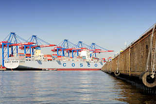 6555 Leerer Schiffsliegeplatz im Hamburger Hafen / Ellerholzhafen; gewaltige Gummifender hngen an der Kaimauer - Containerschiff unter Containerbrcken am Container Terminal Burchardkai.