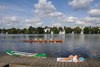 2962 Eine junge Frau hat ihre Kanufahrt auf der Alster unterbrochen und sonnt sich auf dem Holzsteg - ein Ruderboot, Vierer mit Steuermann fhrt vorber - am gegenberliegenden Winterhuder Ufer des Sees kreuzen Segelboote vor dem Ufer der Bellevue.