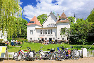 1848 Kulturforum Alte Schwimmhalle Pln; Aussengastronomie - Tische in der Sonne auf der Wiese; Fahrrder am Zaun - blauer Himmel, weisse Wolken